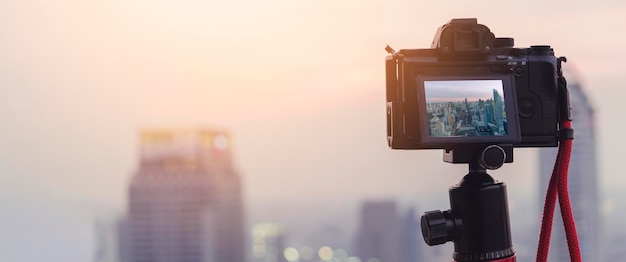 Primo piano della fotocamera sul treppiede che riprende il paesaggio urbano al tramonto con il concetto di idee di viaggio della città del centro urbano di sfondo