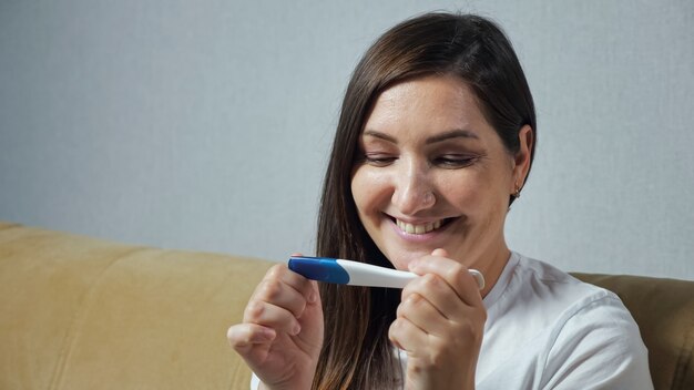 Primo piano della giovane donna che esamina felicemente il test di gravidanza.