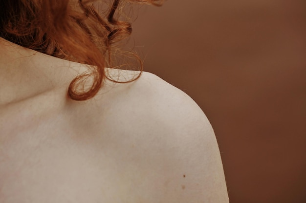 Primo piano della giovane donna con capelli ricci rossi che raggiungono la sua spalla isolata su fondo marrone