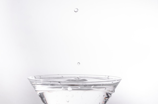 Primo piano della goccia d'acqua che cade in un bicchiere su sfondo bianco