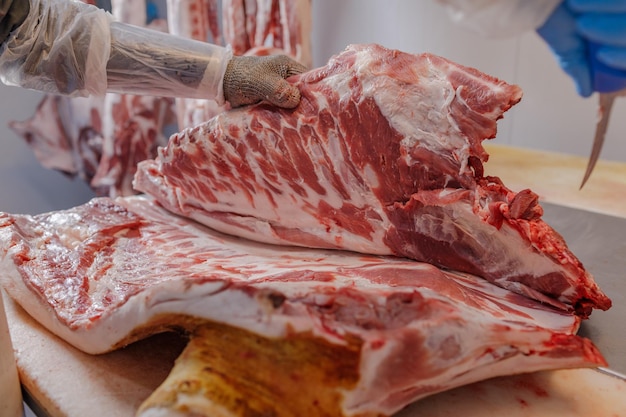 Primo piano della lavorazione della carne nell'industria alimentare un lavoratore taglia carne di maiale cruda il concetto di prodotti a base di carne