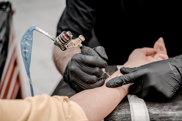 Primo piano della macchinetta del tatuaggio. Tatuaggio. Uomo che crea un'immagine sulla sua mano da un tatuatore professionista.