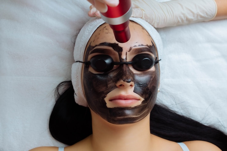 Primo piano della mano dei cosmetologi che fa il peeling del carbonio dell'hardware da una giovane donna graziosa del cliente in cassaforte