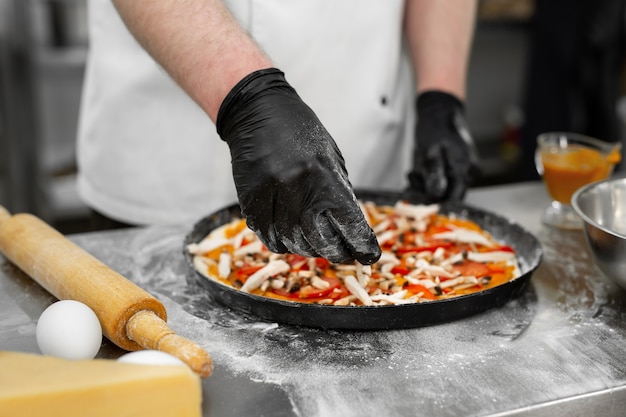 Primo piano della mano del cuoco che stende la carne sull'impasto