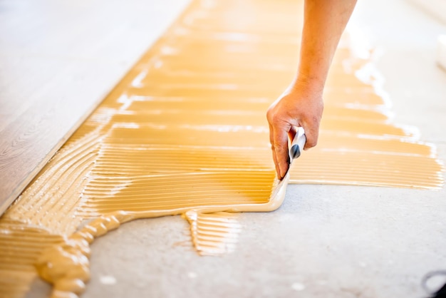 Primo piano della mano del lavoratore che aggiunge colla durante l'installazione del parquet