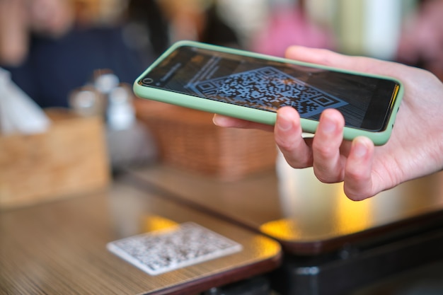 Primo piano della mano dell'ospite che ordina il pasto al ristorante durante la scansione del codice qr con il telefono cellulare per il menu online.