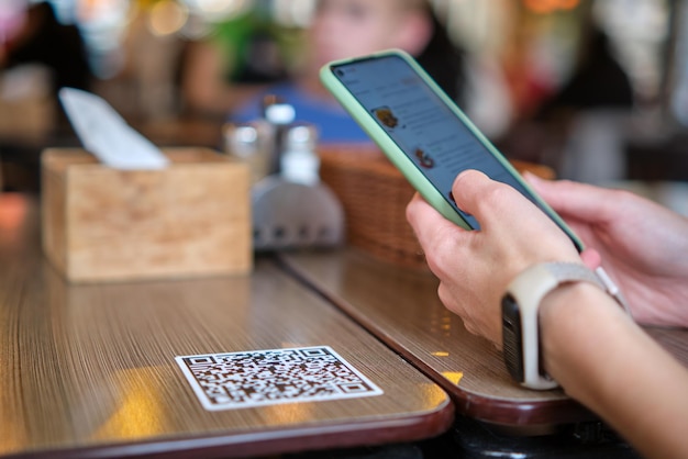 Primo piano della mano dell'ospite che ordina il pasto nel ristorante durante la scansione del codice QR con il telefono cellulare per il menu online