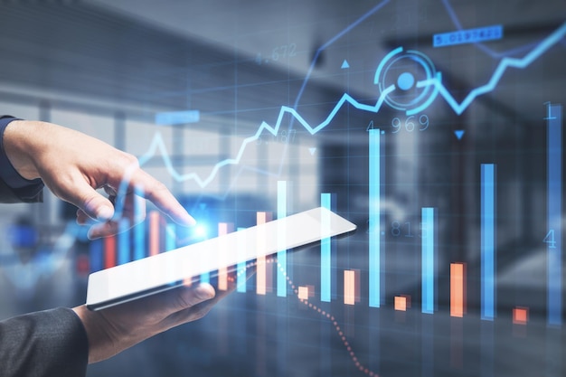 Primo piano della mano dell'uomo d'affari che punta al tablet con grafico forex incandescente creativo su sfondo interno ufficio sfocato Dispositivo commerciale investimento finanziario e concetto tecnologico Doppia esposizione