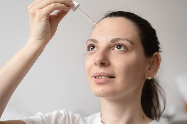 Primo piano della mano della donna bianca che applica olio di olio essenziale o siero per la pelle Concetto di cura di sé