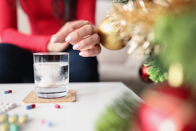 Primo piano della mano della donna che mette la compressa in acqua, reazione chimica in vetro. Capsule sul tavolo, farmaci per il mal di testa, antidolorifici. Malessere, salute, natale, concetto di capodanno. Sfondo sfocato