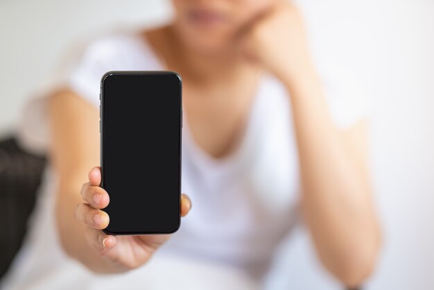 Primo piano della mano della donna che tiene e mostra lo smartphone nero dello schermo in bianco.