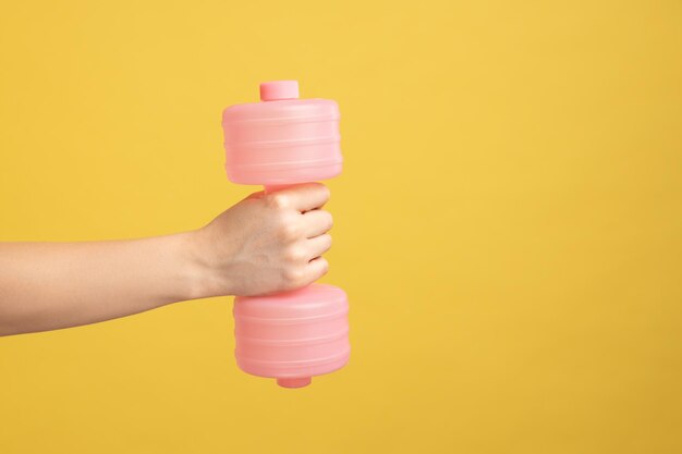 Primo piano della mano della donna che tiene l'attrezzatura rosa del manubrio per il fitness e l'attività di allenamento a casa