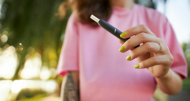 Primo piano della mano della donna che tiene una sigaretta elettronica. Sistema di tabacco IQOS.