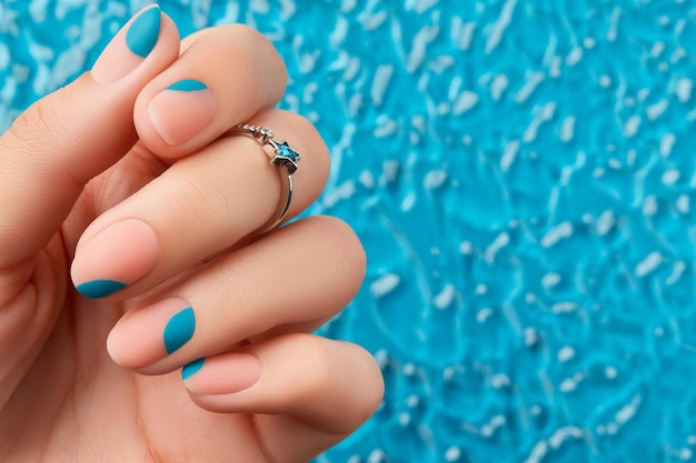 Primo piano della mano della donna con la manicure estiva su sfondo blu Tendenze del design del manicure