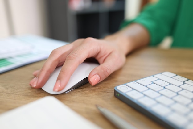 Primo piano della mano della donna d'affari che tiene il mouse del computer sulla scrivania dell'ufficio con tastiera e documenti