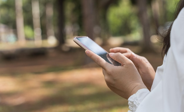 Primo piano della mano della donna dell'immagine utilizzando il telefono cellulare nel parco Ricerca o concetto di social network