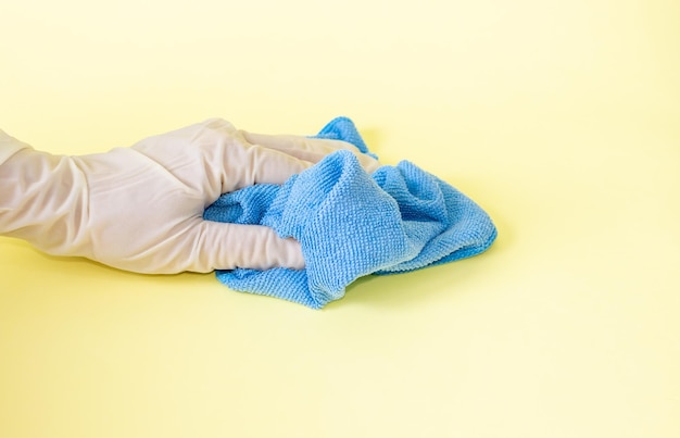 primo piano della mano della donna nel guanto chirurgico tiene in mano un tovagliolo di colore blu su sfondo giallo