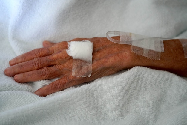 Primo piano della mano della soluzione salina del paziente anziana nella stanza d'ospedale