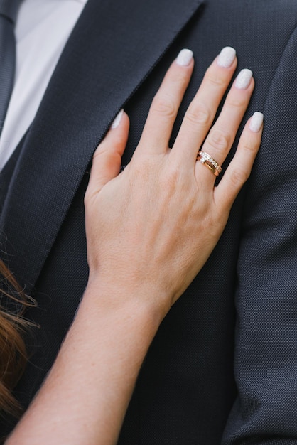 Primo piano della mano della sposa con un anello di fidanzamento sul petto dello sposo