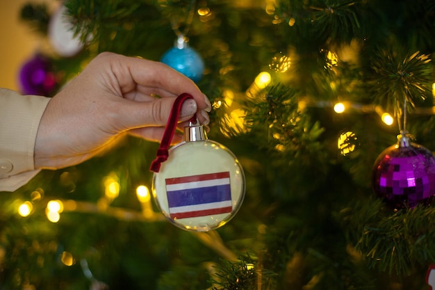 Primo piano della mano delle ragazze che tiene una palla di Natale per un abete con la bandiera della Thailandia Capodanno in Thailandia Biglietto di auguri per le vacanze di Capodanno con copia spazio per il testo Decorazione della casa per la celebrazione