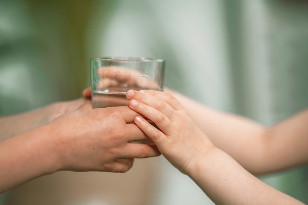 Primo piano della mano di un uomo che dà un bicchiere di acqua fresca filtrata a un bambino