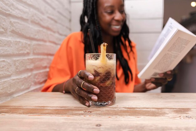 Primo piano della mano di una donna che legge un libro e tiene in mano un bicchiere di succo fresco