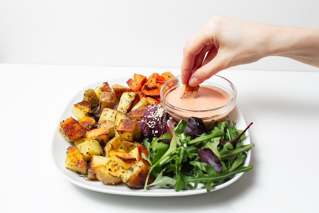 Primo piano della mano femminile che immerge le patate arrosto in salsa su fondo bianco