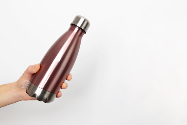 Primo piano della mano femminile, che tiene la bottiglia di acqua termica eco in acciaio inox riutilizzabile con mockup