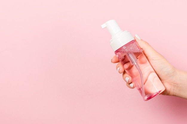 Primo piano della mano femminile che tiene uno spray di prodotto cosmetico su sfondo rosa con spazio di copia.