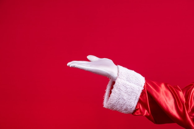 Primo piano della mano guantata di Babbo Natale che mostra gesticolando su sfondo rosso. Tempo festivo per felice anno nuovo, buon Natale, tradizionale celebrazione stagionale.