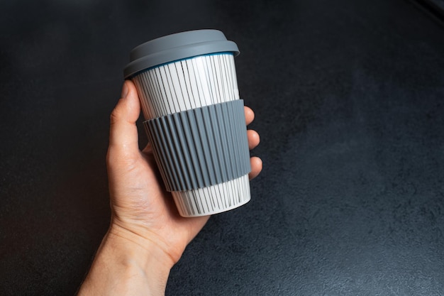 Primo piano della mano maschile che tiene una tazza di ceramica per il caffè da asporto su sfondo nero