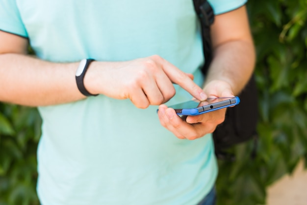 Primo piano della mano maschile con un fitness tracker e uno smartphone all'aperto.