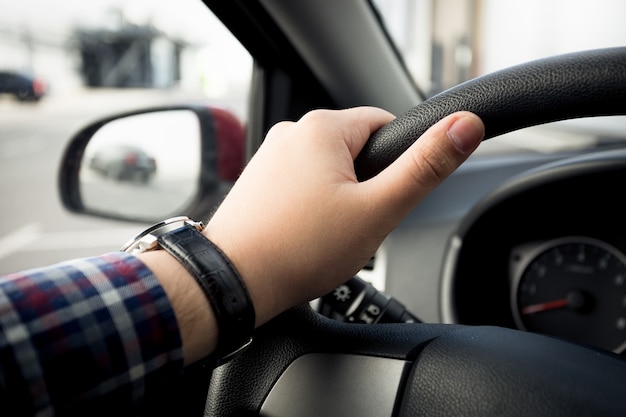 Primo piano della mano maschile negli orologi che tengono il volante dell'auto