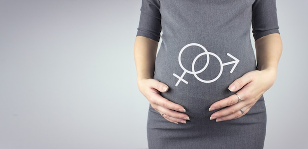 Primo piano della pancia della donna incinta con ologramma simbolo di genere maschile e femminile. Gravidanza, concetto di maternità.