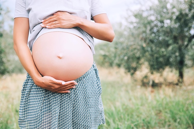 Primo piano della pancia incinta in natura all'aperto spazio di copia Donna incinta tiene le mani sulla pancia su sfondo naturale di erba verde Aspettativa di gravidanza nascita di nuovi concetti di vita