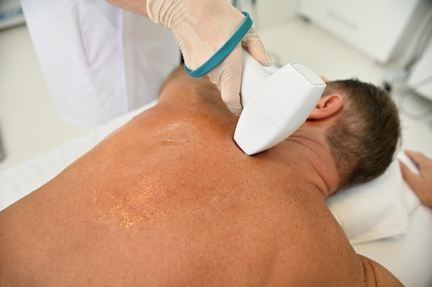 Primo piano della parte posteriore del cliente maschio della spa benessere che riceve un trattamento professionale per il corpo con moderne apparecchiature mediche - Apparecchio per la cavitazione ultrasonica del corpo. Sollevamento delle onde radio presso la clinica termale.