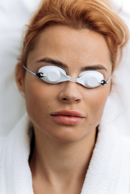 Primo piano della paziente che indossa occhiali protettivi sdraiata sul divano dopo la procedura di depilazione in clinica