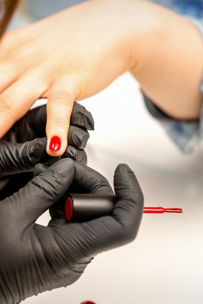 Primo piano della pittura della vernice del manicure di un maestro del manicure che indossa guanti neri di gomma che applicano il varn rosso