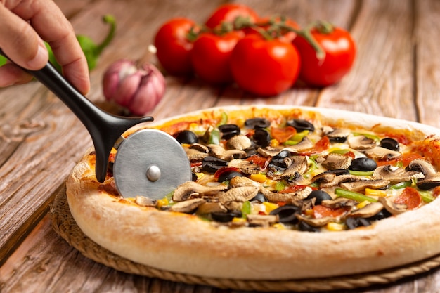 Primo piano della pizza di taglio a mano con verdure e peperoni su legno