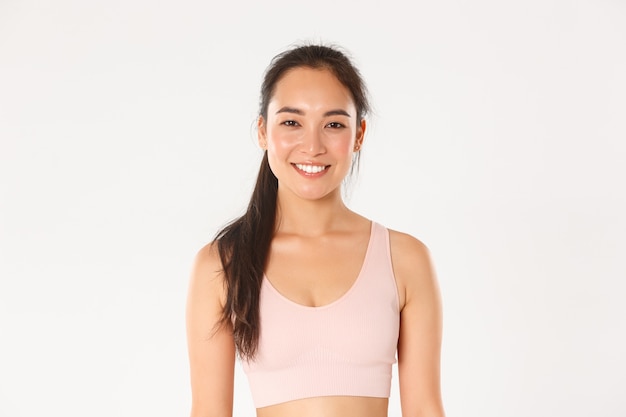 Primo piano della ragazza asiatica attraente sorridente di forma fisica, cliente femminile della palestra o sportiva in reggiseno sportivo alla ricerca pronta per l'allenamento, iniziare l'allenamento.