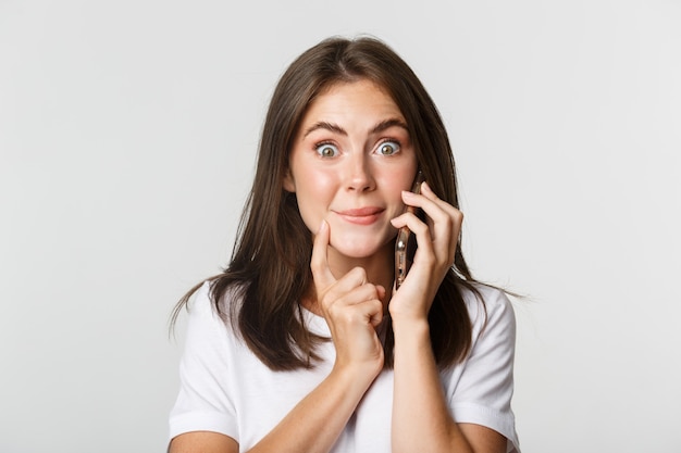 Primo piano della ragazza sorridente incuriosita che parla sullo smartphone con l'espressione tentata.