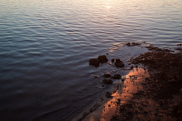 Primo piano della riva del fiume con il riflesso del tramonto.