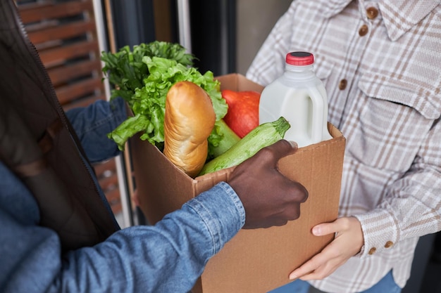 Primo piano della scatola della tenuta della donna con i generi alimentari all'aperto con l'uomo di consegna