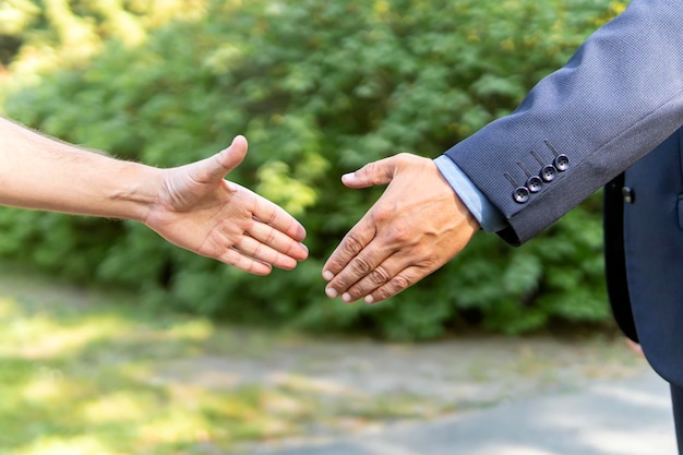 Primo piano della stretta di mano di saluto sullo sfondo del parco. Incontrare gli amici nella natura. imprenditore e dipendente. capo e subordinato. Agricoltore e uomo d'affari che si stringono la mano