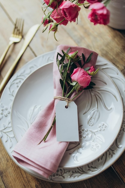 Primo piano della tavola con tovagliolo di lino rosa e rametto di rosa