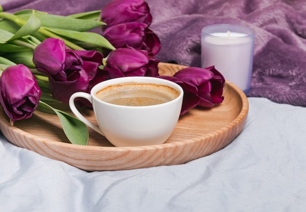 Primo piano della tazza di caffè, dei tulipani e della candela