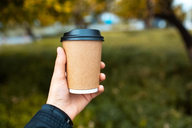 Primo piano della tazza di carta per il caffè da asporto in mano maschile sullo sfondo all'aperto