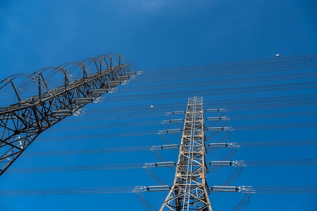 Primo piano della torre di comunicazione e satellitare con cavi di collegamento che trasferiscono elettricità e rete in piedi sotto il cielo blu chiaro