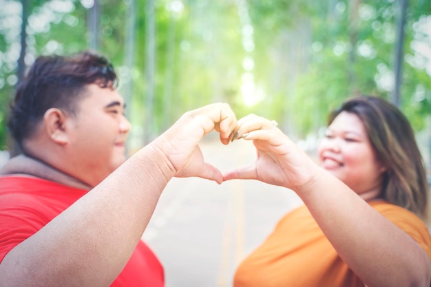 Primo piano delle coppie asiatiche grasse che fanno il segno della mano di amore