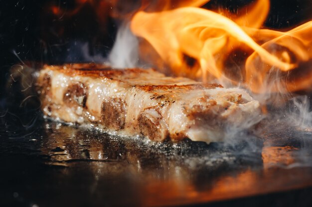 Primo piano delle costole di carne di maiale della carne di maiale marinata arrosto del BBQ sulla griglia ardente calda